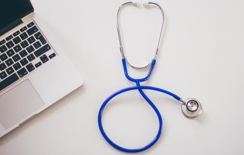 A stethoscope next to a laptop on a white desk