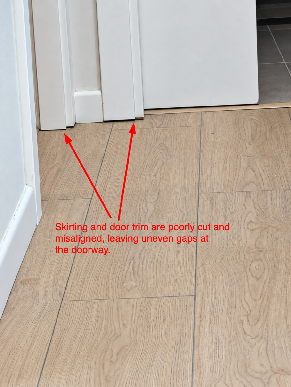 Skirting board and door trim at a doorway, cut short and misaligned, leaving uneven gaps.