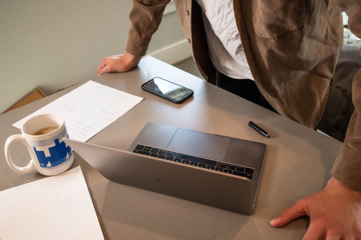 A person at a desk with a laptop, a phone and paperwork