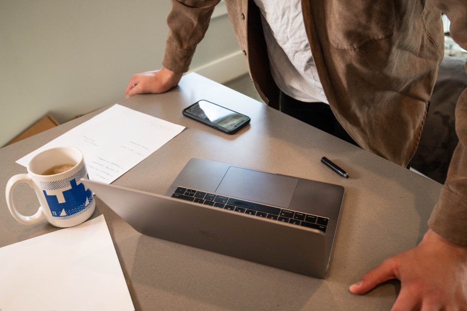 A person at a desk with a laptop, a phone and paperwork