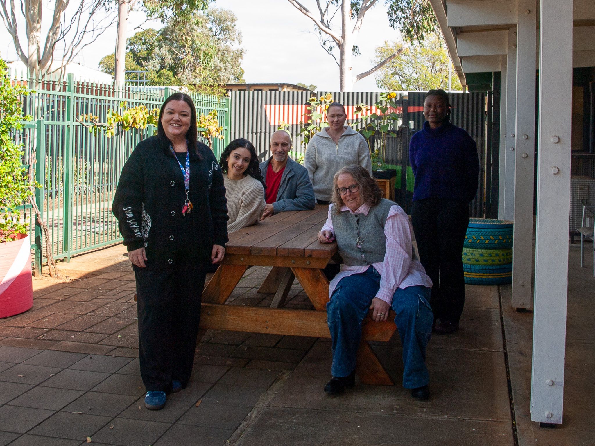Photo of smiling staff members standing outside sitting on a bench.