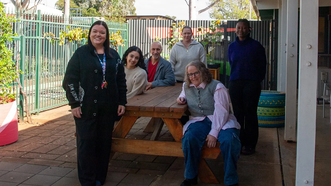 Photo of smiling staff members standing outside sitting on a bench.
