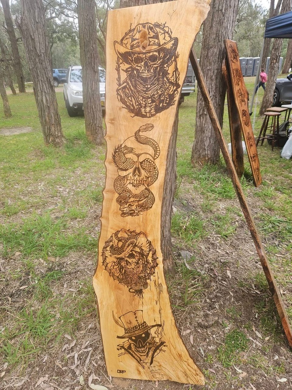 Tall natural-edged timber slab with a vertical series of dark skull illustrations