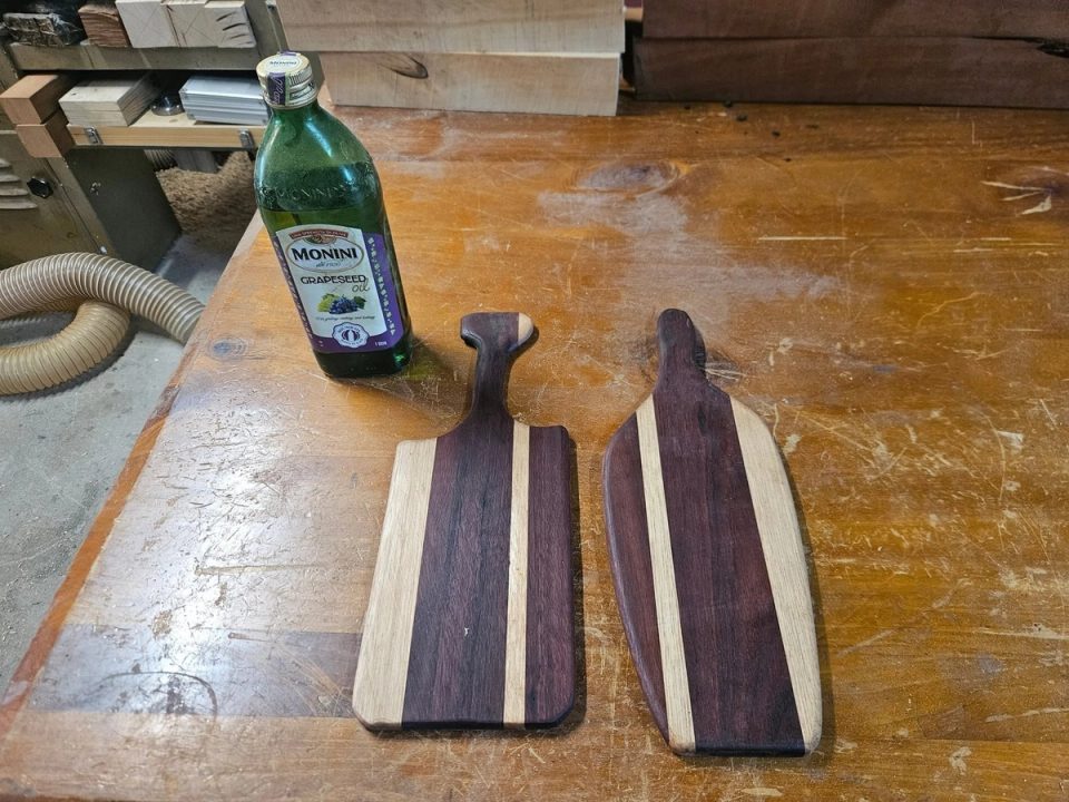 Two paddle-shaped timber serving boards with dark and light stripes on a workbench