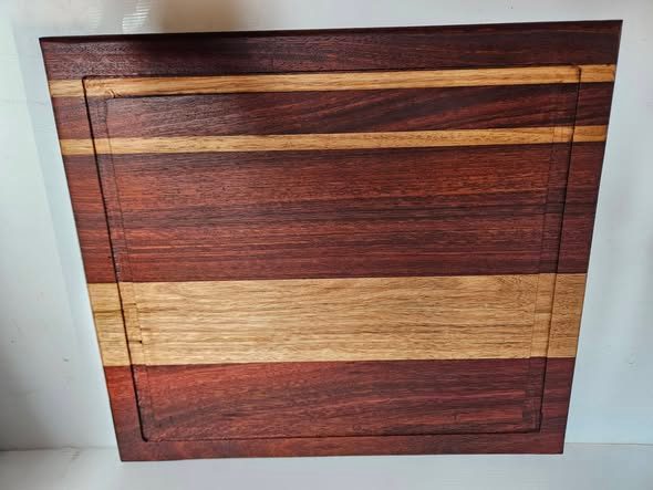 Rectangular red-brown chopping board with golden timber stripes and a routed perimeter groove