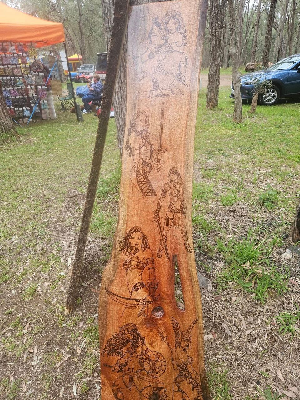 Tall timber slab displayed outdoors with burned figure illustrations along its face