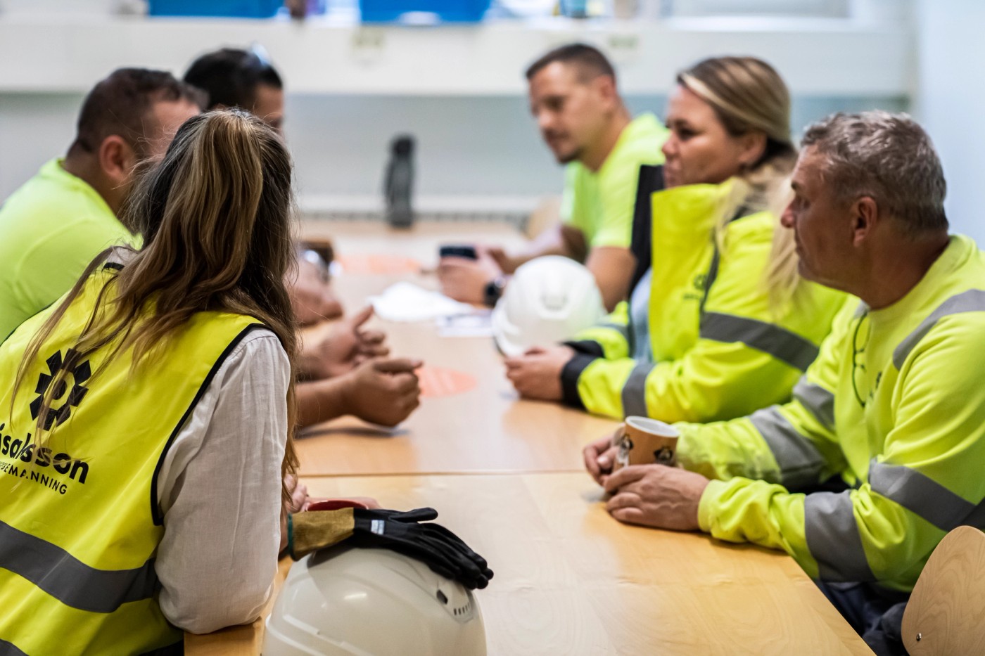 En grupp människor i gula arbetskläder diskuterar vid ett bord 
