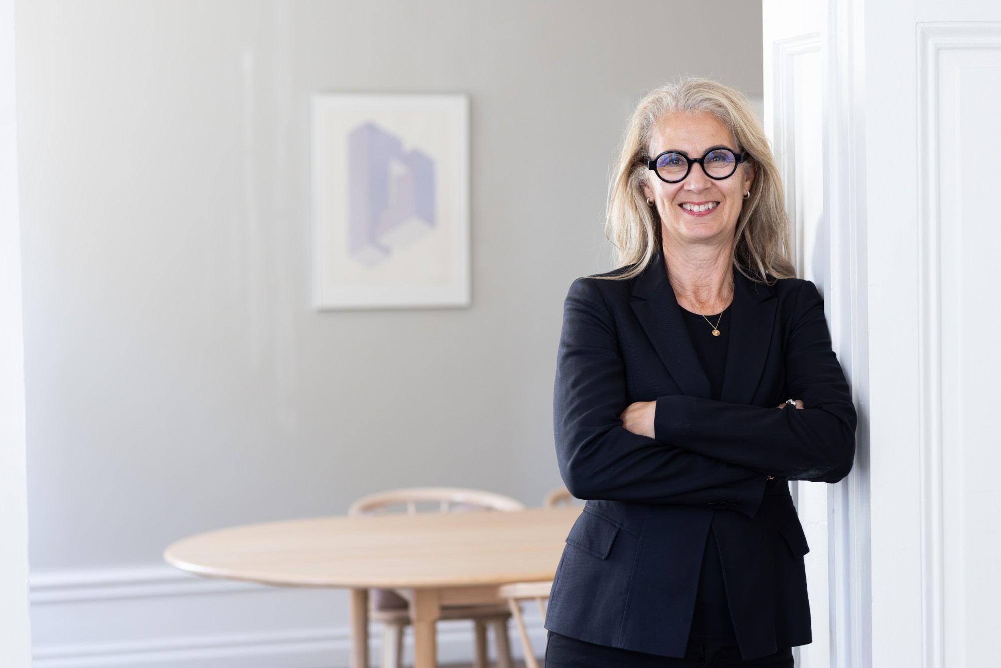Leende kvinna i vit blus står vid höga fönster i en ljus lokal