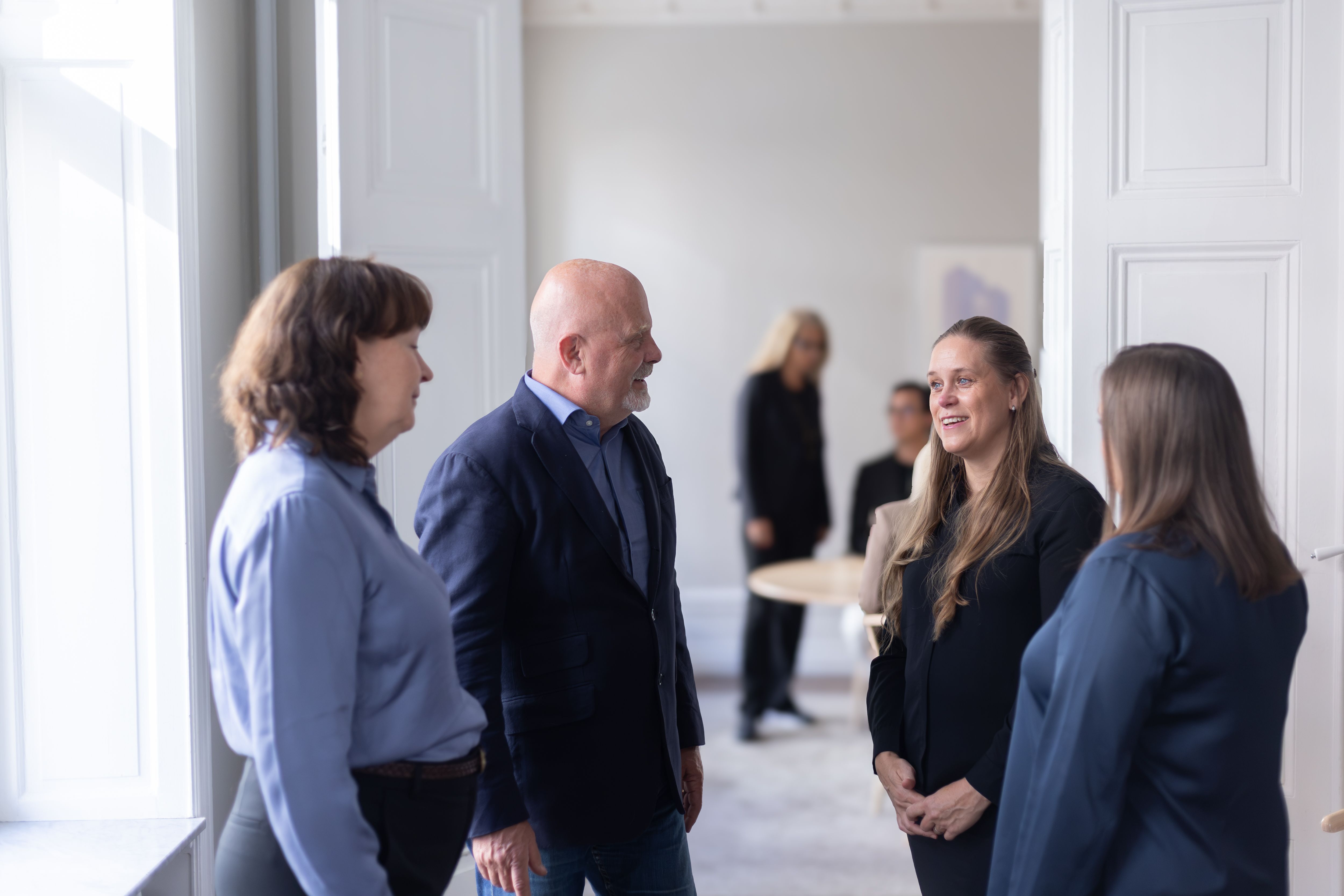 Fyra personer samtalar på en innergård framför ett rött bostadshus