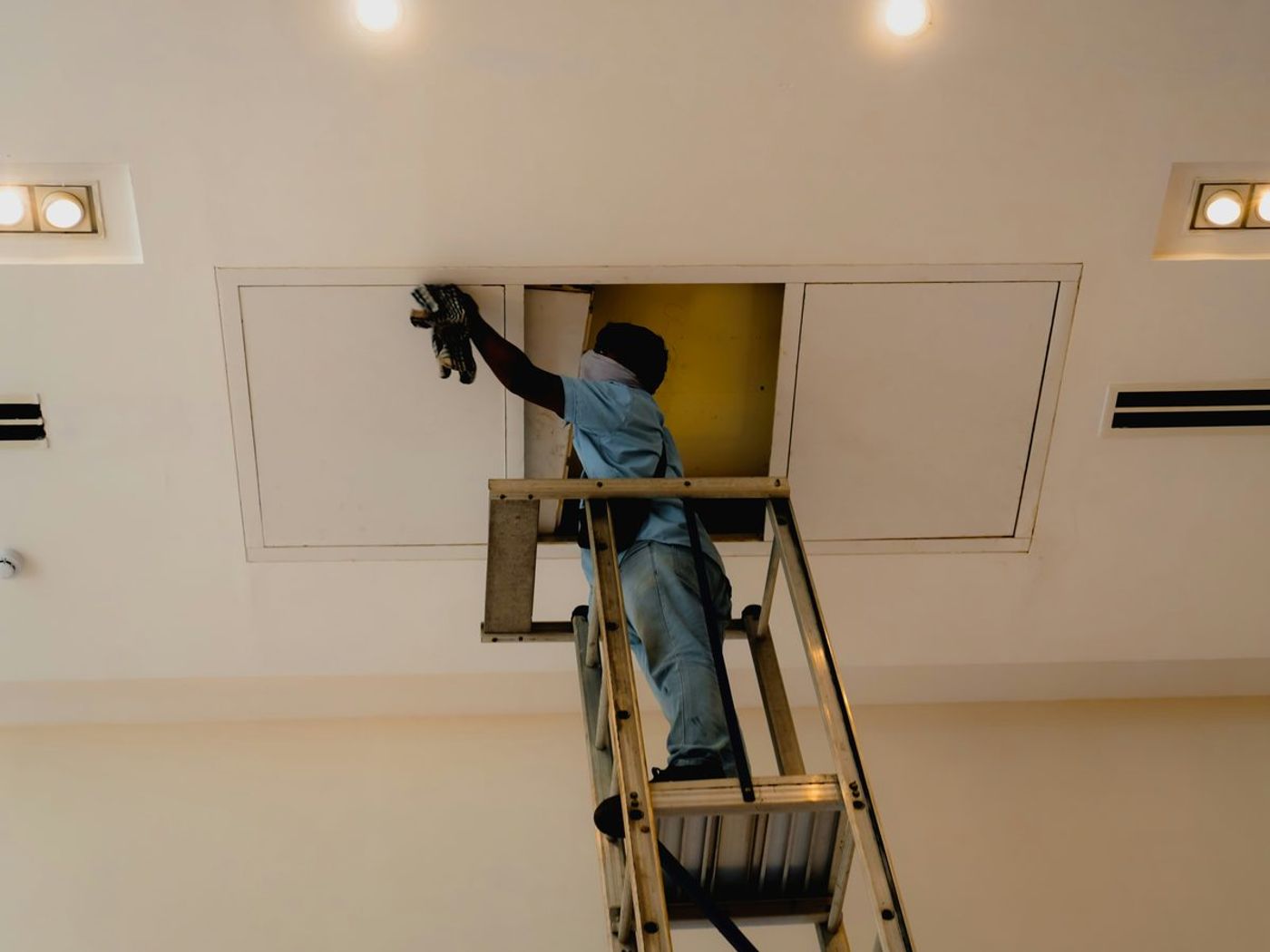 Technician on a ladder working at a ceiling access panel