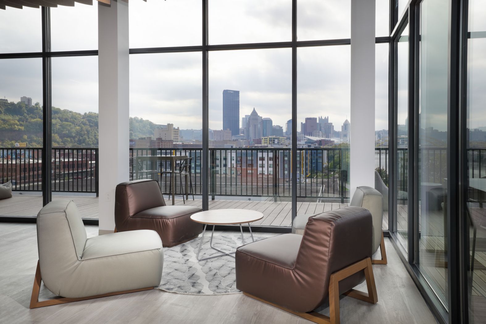 Sixth floor club room with a fireplace, chairs, couches, and a view of the strip district and downtown Pittsburgh