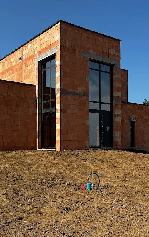 Maison contemporaine en briques au stade du gros œuvre avec grandes baies vitrées