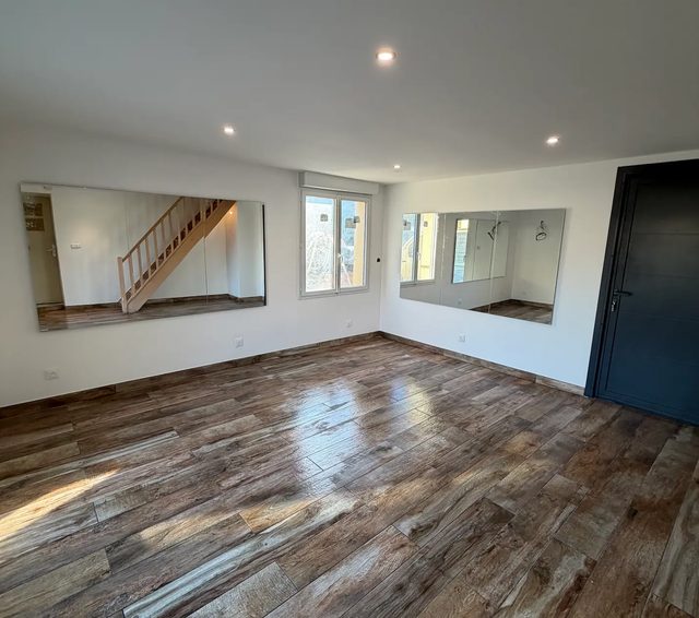 Pièce de vie rénovée avec escalier en bois, baie vitrée coulissante et carrelage imitation bois