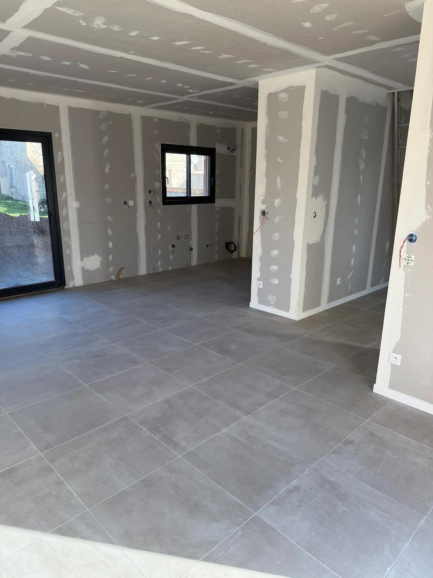 Intérieur de la maison en cours de finition avec carrelage gris, escalier et cloisons blanches