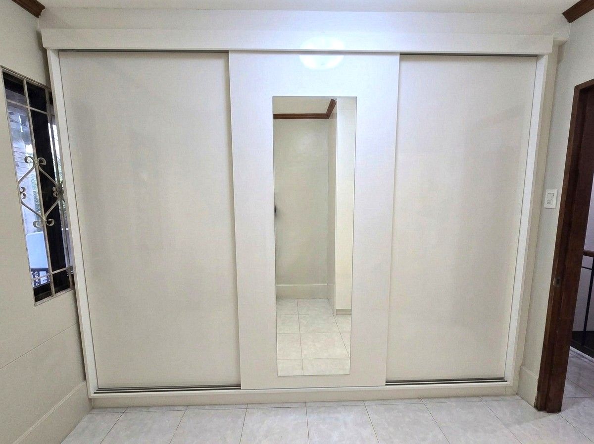 A white built-in wardrobe with a sliding mirror-panel door, two wide hanging sections, four deep drawers, and warm LED lighting inside. Made to fit your wall.