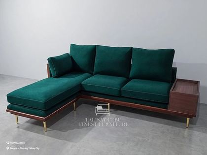 This mid-century modern sectional pairs a rich emerald green velvet upholstery with a warm walnut-toned wood base and brushed brass legs. Fine contrast piping outlines each cushion, adding a tailored finish.