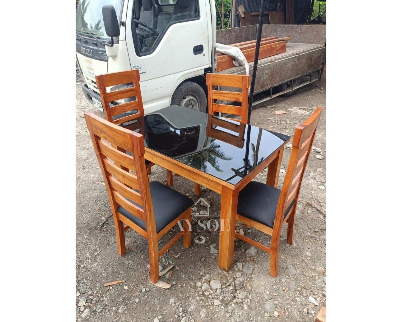 A 4-seater dining set with a solid wood frame, a sleek black glass tabletop, and four ladder-back chairs with black cushioned seats. Sturdy, wipe-clean, made to order.