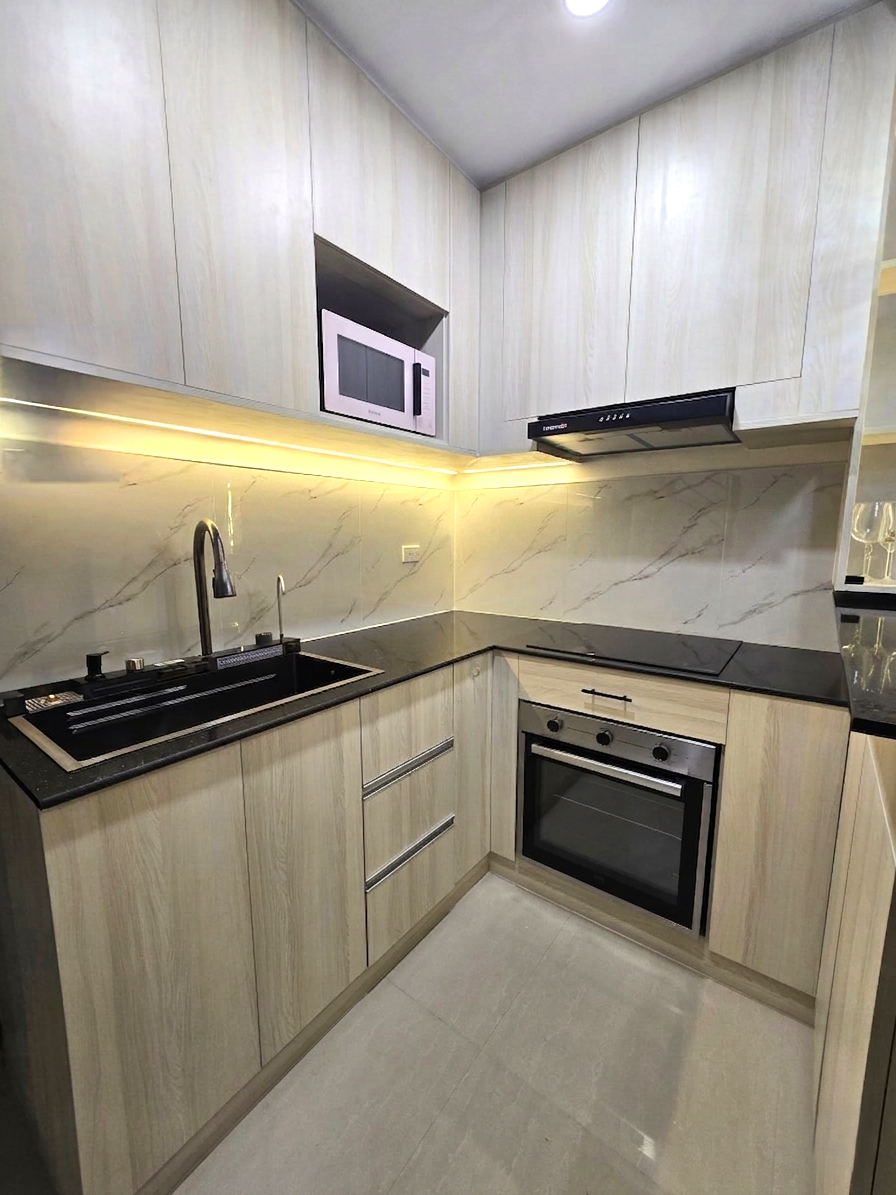 A compact light oak kitchen with a marble-look backsplash, breakfast bar, and lit glass display cabinet.