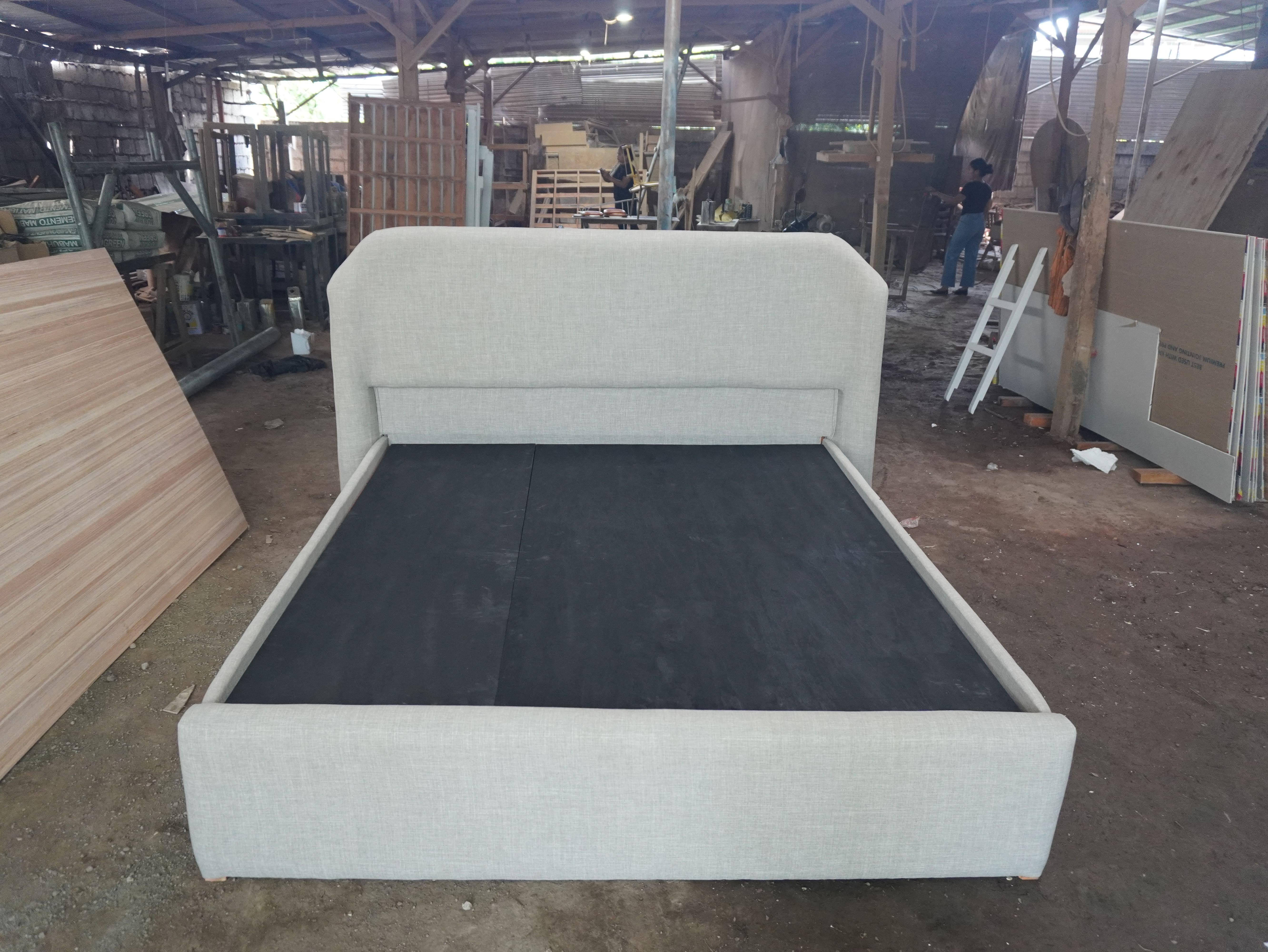 A clean, minimalist upholstered bed in light woven linen-style fabric, with a soft rounded headboard and a fully wrapped, low-profile frame. Calm, neutral, and easy to style.