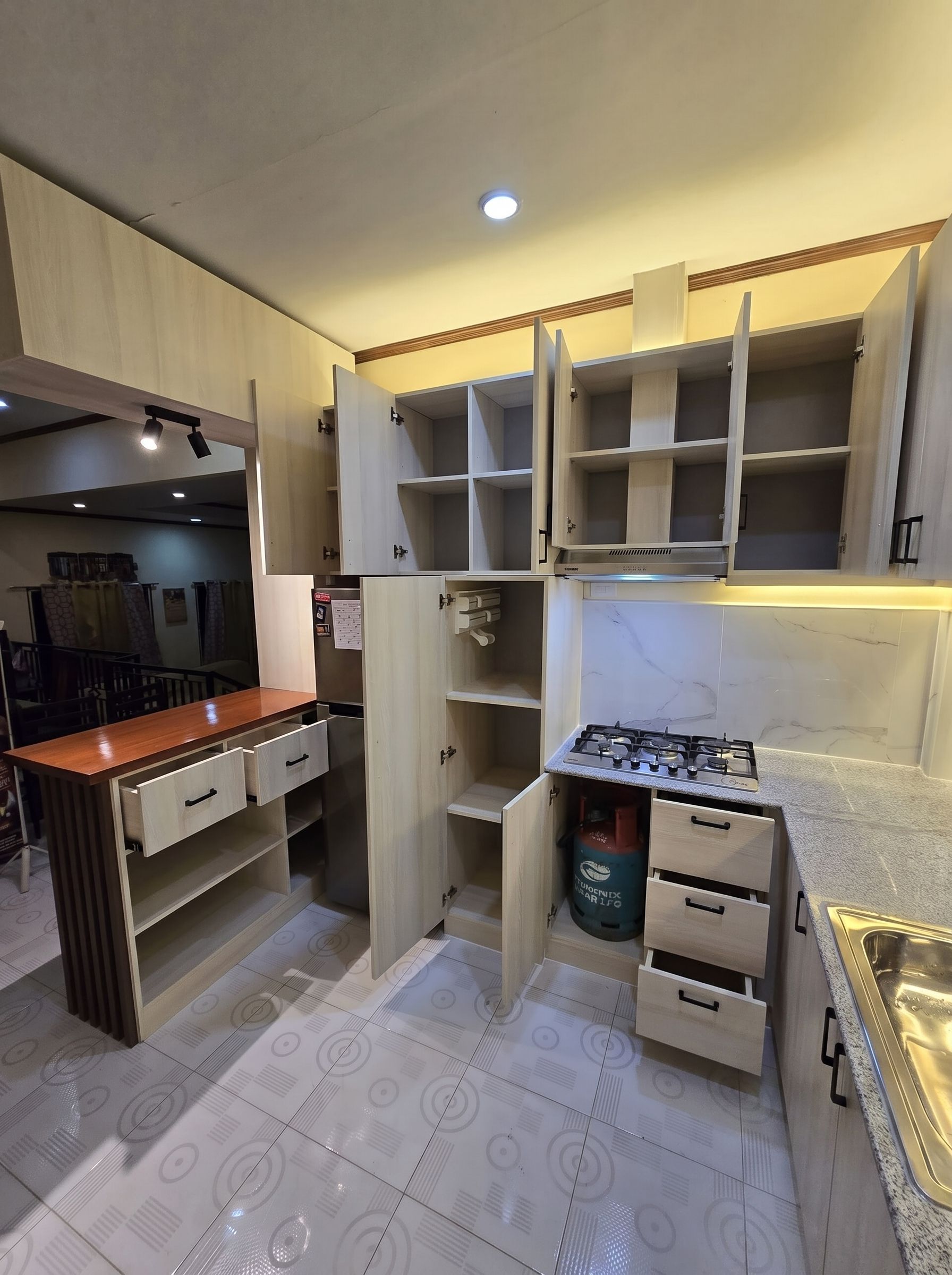 A light oak L-shaped kitchen with a marble-look backsplash, wood breakfast bar, and lit glass display cabinets.