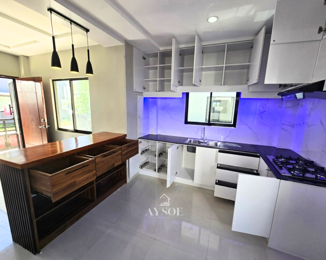 A modern L-shaped kitchen set with glossy white cabinets, a dark countertop, a marble-look backsplash, and a wood island counter with drawers. Plenty of storage in a clean, bright design.