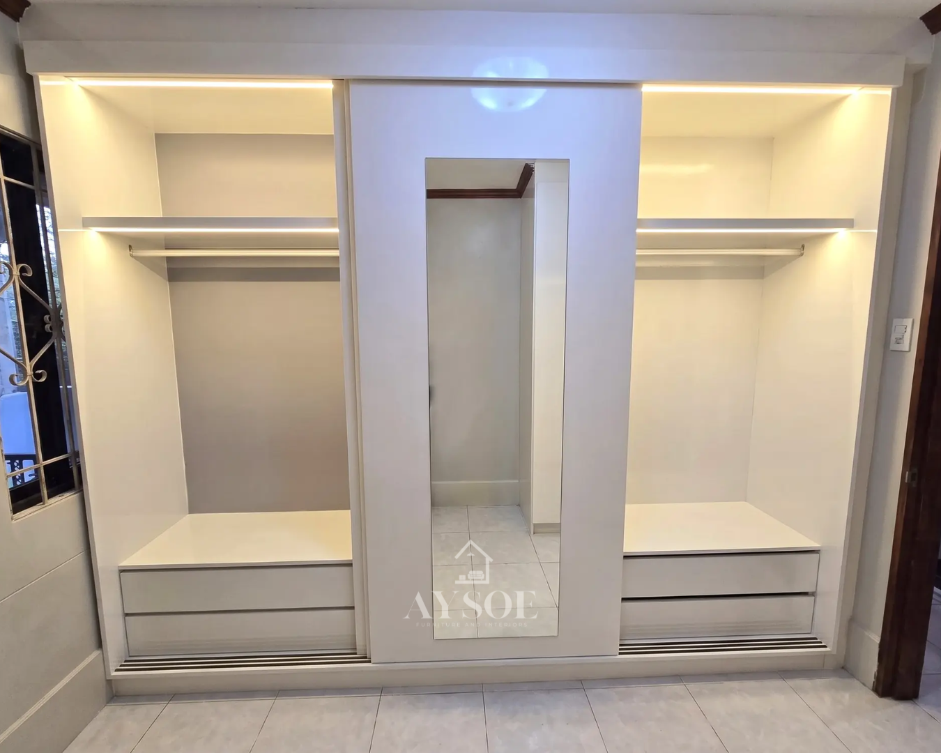 A white built-in wardrobe with a sliding mirror-panel door, two wide hanging sections, four deep drawers, and warm LED lighting inside. Made to fit your wall.