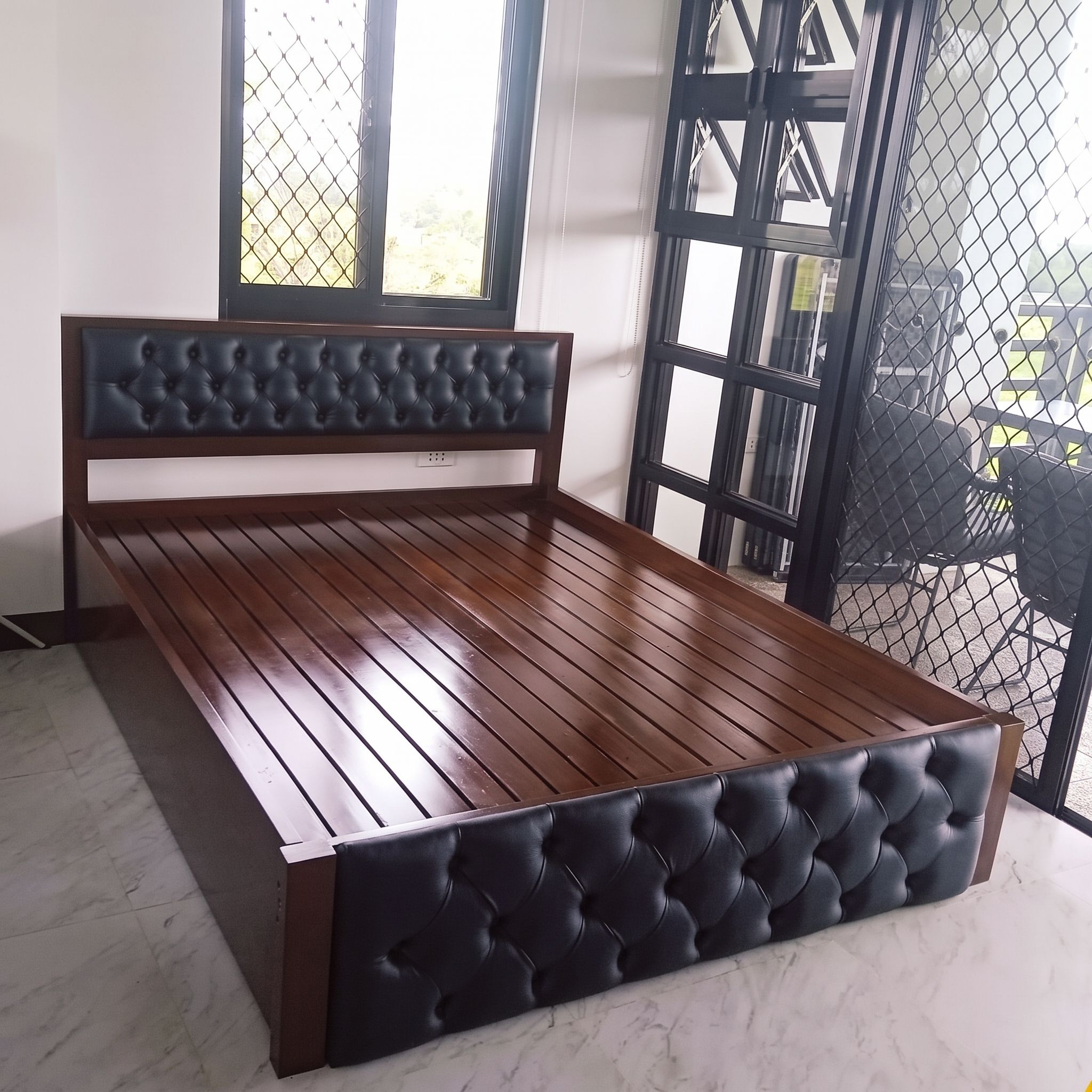A solid wood bed in a rich, glossy dark walnut finish, with a black button-tufted leatherette headboard panel, a matching tufted footboard, and a sturdy slatted base. Bold, classic, and built to last.