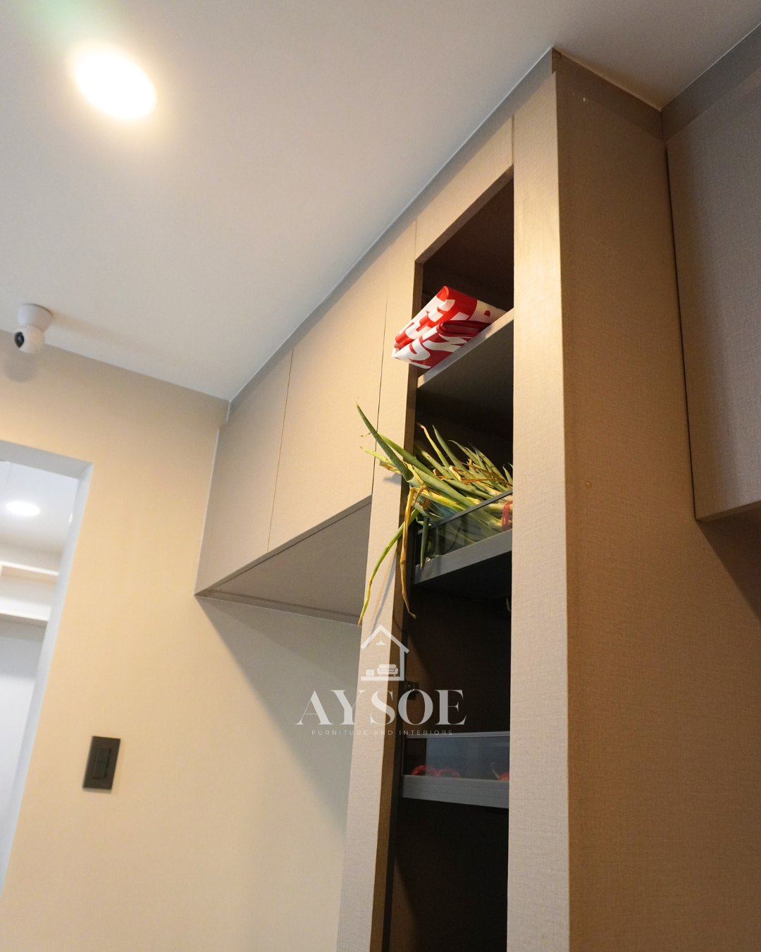 A custom taupe linen-finish storage set with a tall pull-out pantry with six wire baskets and handleless overhead cabinets. Organized storage for kitchens and utility areas.