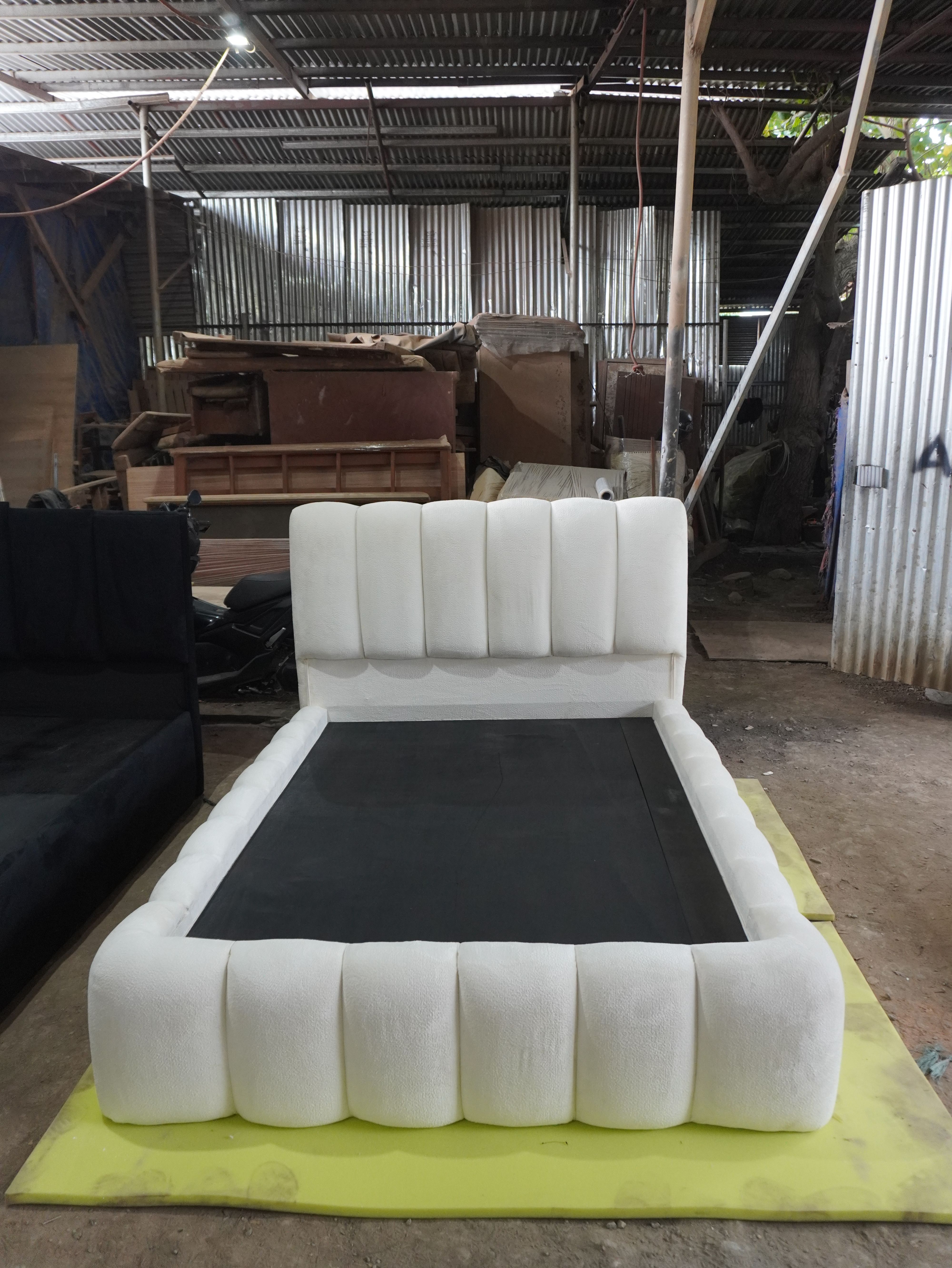 A soft, sculptural bed in ivory bouclé fabric, with a tall rounded channel headboard and thick pillow-style channels wrapping the whole frame. Cozy, modern, and a real statement piece.
