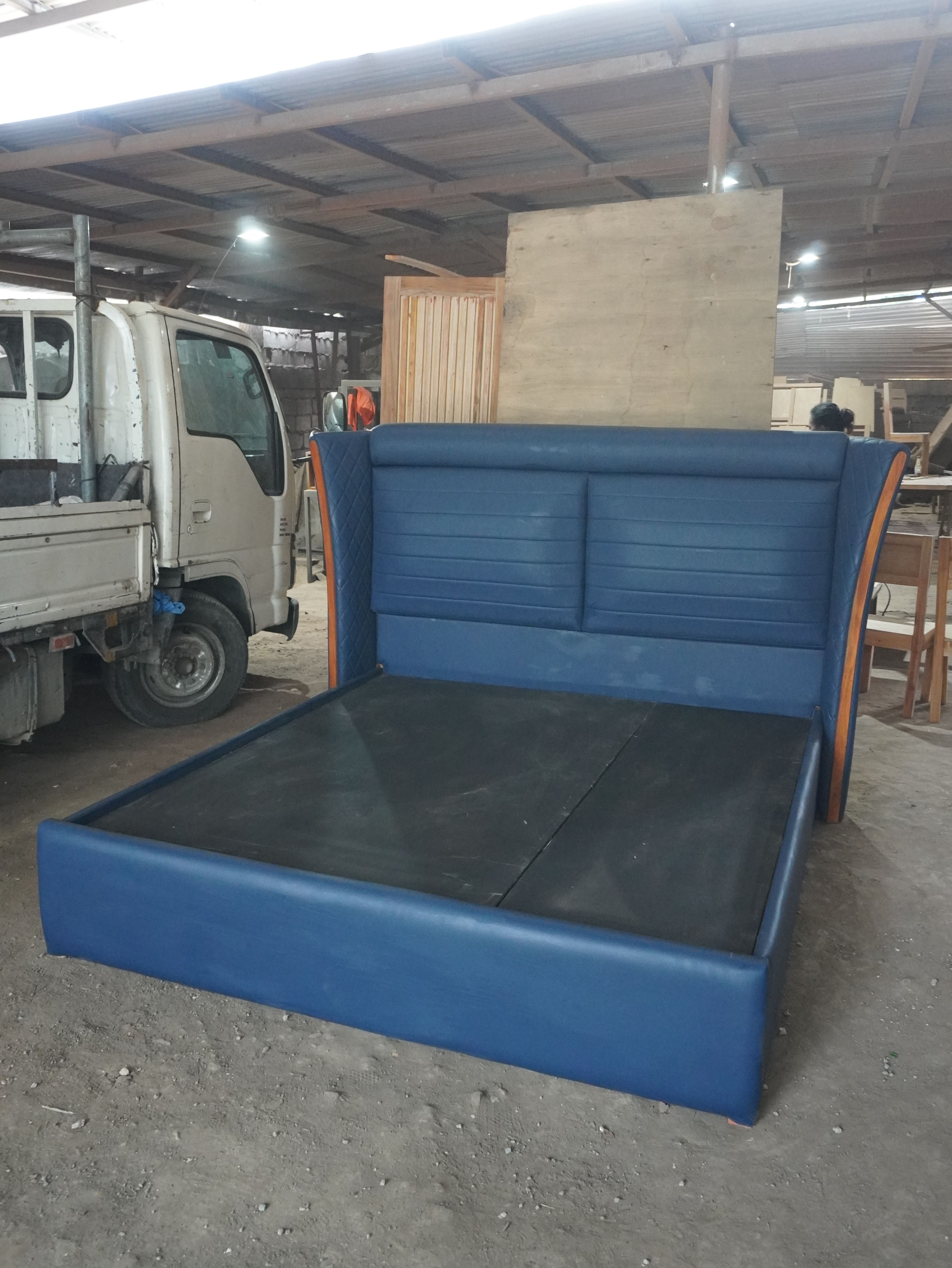 A bold navy blue leatherette bed with a tall curved wingback headboard, horizontal channel panels, and quilted diamond-stitch wings edged in warm wood. Clean, fully wrapped frame with a solid platform base.