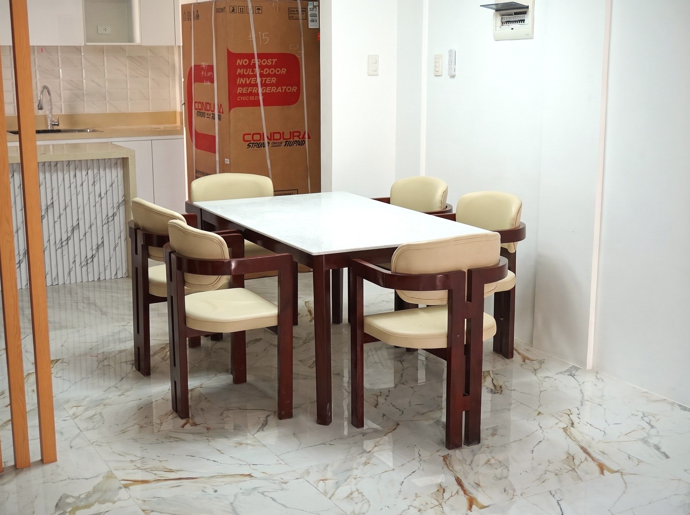 A six-seater dining set with a white quartz-top table and cream leather armchairs on dark mahogany-finish wood frames.