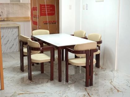 A six-seater dining set with a white quartz-top table and cream leather armchairs on dark mahogany-finish wood frames.