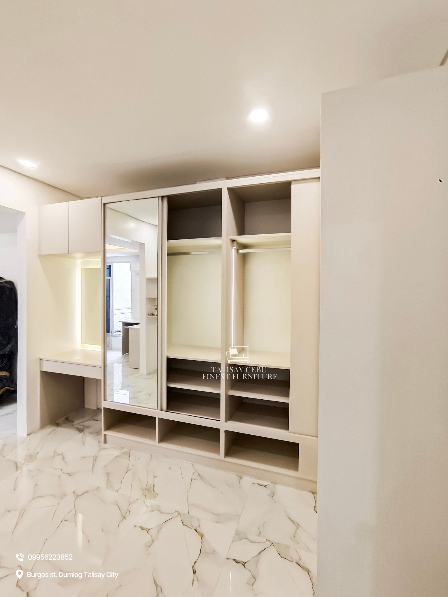 a custom floor-to-ceiling cream wardrobe with sliding mirror doors, open shoe cubbies, and a built-in vanity with drawer and overhead storage.