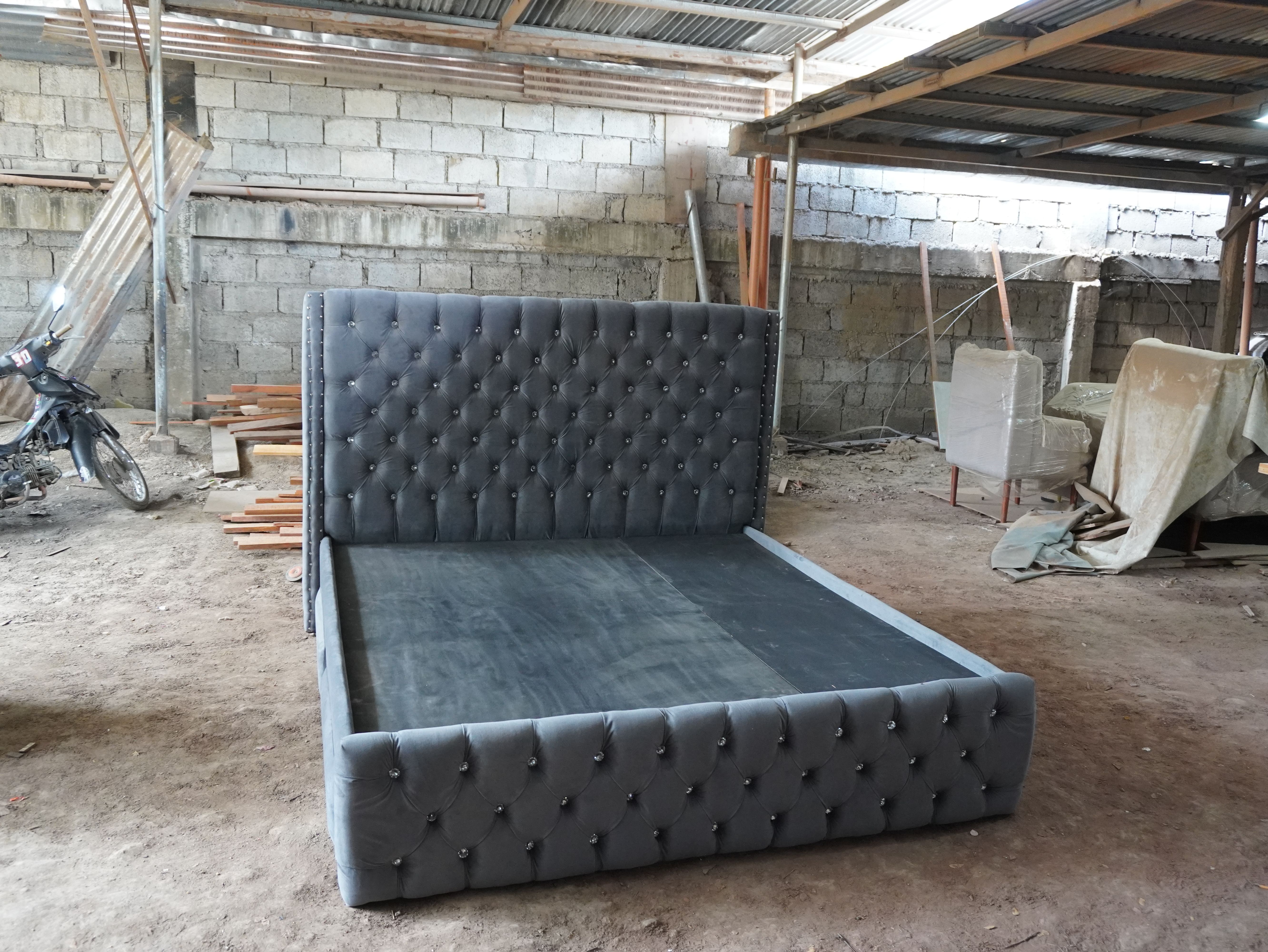 A glamorous bed in charcoal gray velvet-style fabric, with a tall wingback headboard, deep tufting set with sparkling crystal buttons, and nailhead trim. Four upholstered drawers give you built-in storage.
