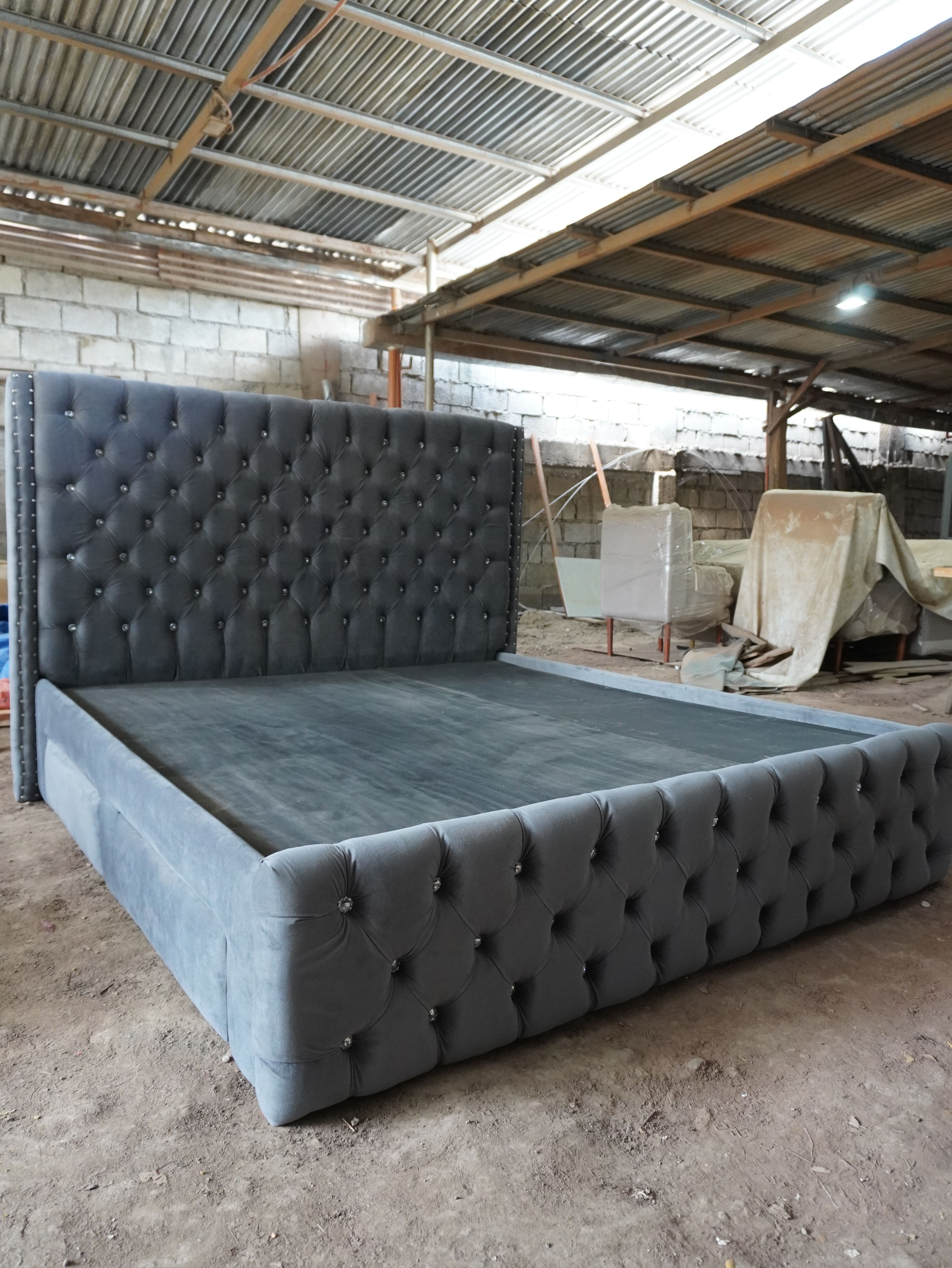A glamorous bed in charcoal gray velvet-style fabric, with a tall wingback headboard, deep tufting set with sparkling crystal buttons, and nailhead trim. Four upholstered drawers give you built-in storage.