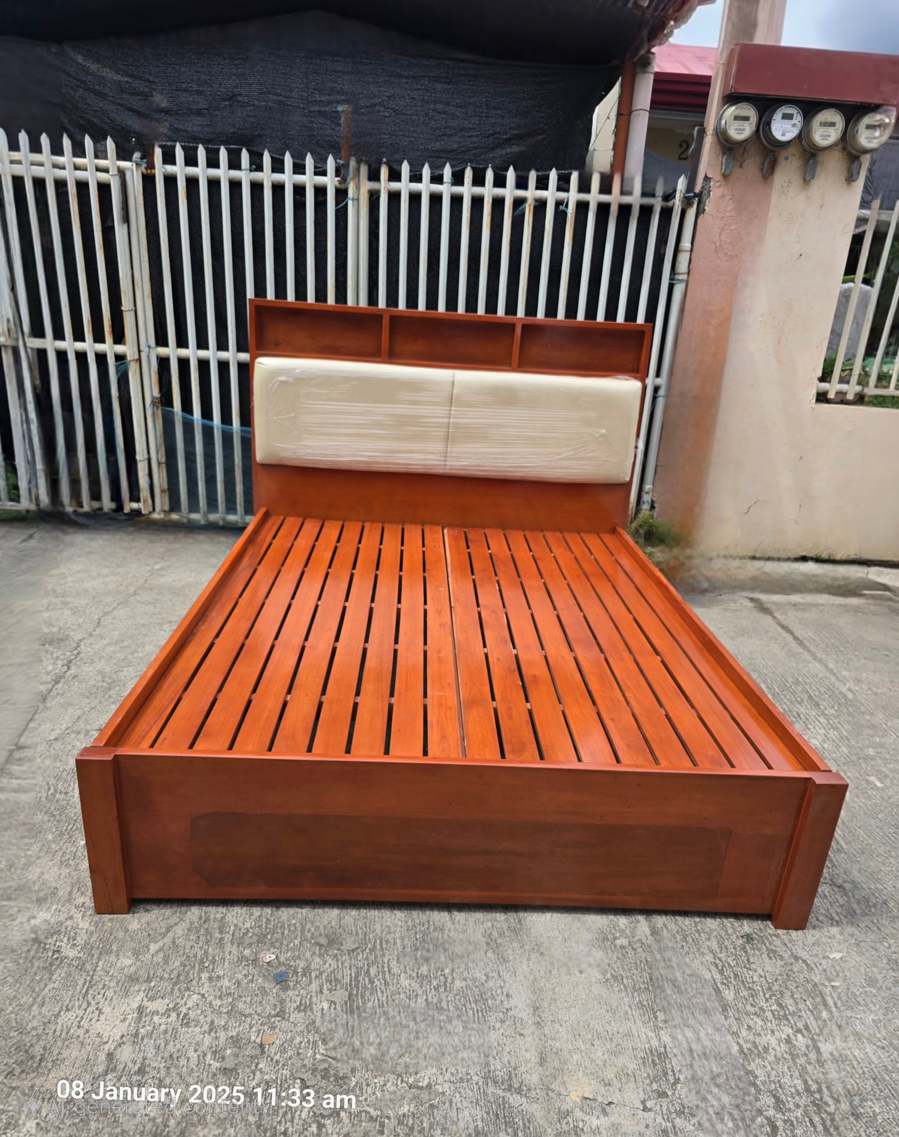 A solid wood bed in a rich cherry finish, with a built-in shelf headboard for books, lamps, and a phone, and cream padded panels for comfortable back support. Clean lines, warm tones, and a sturdy frame.