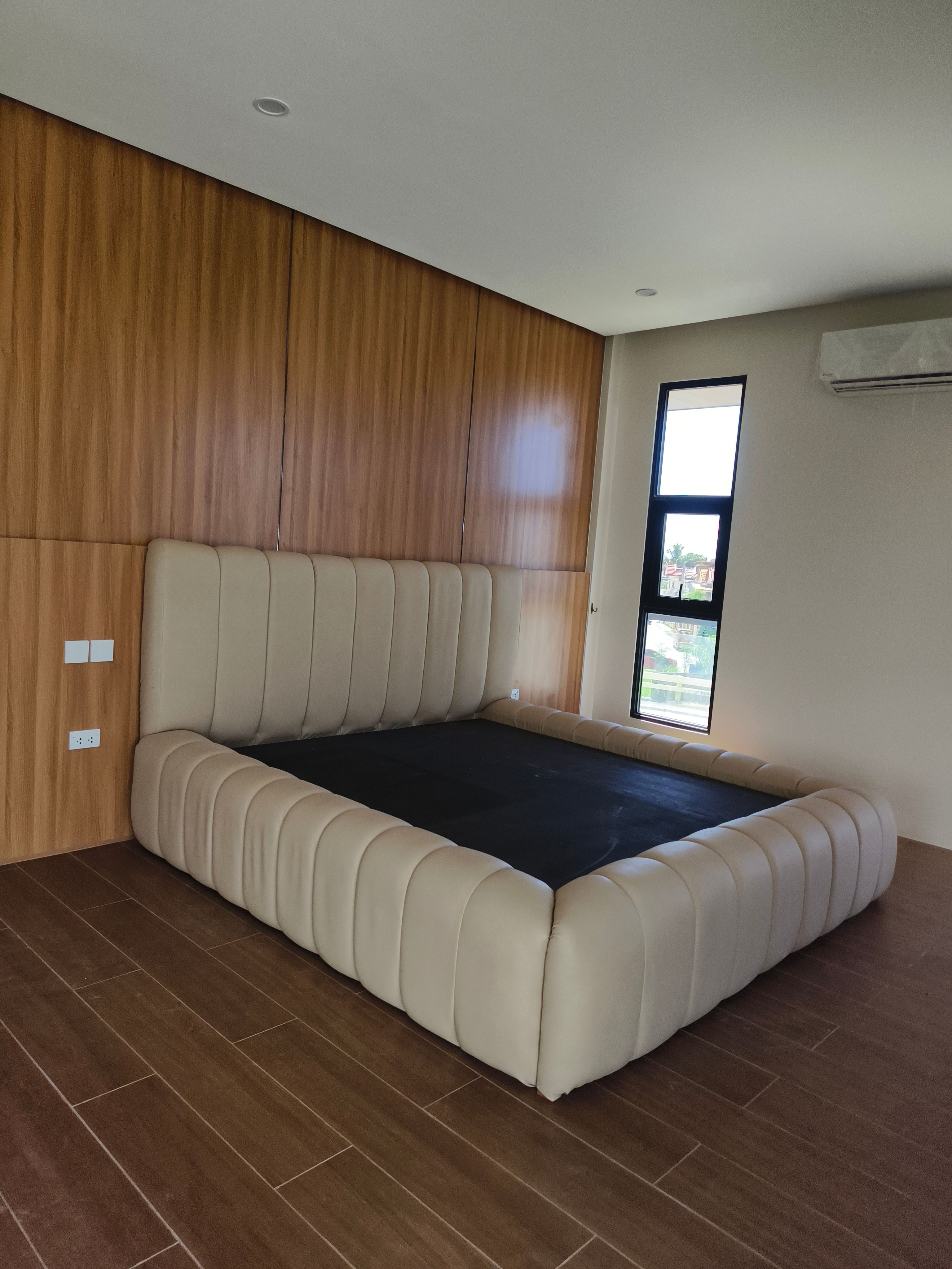 A soft, sculptural bed in smooth cream leatherette, with a tall wide channel headboard and thick pillow-style channels wrapping the whole frame. Plush, modern, and easy to wipe clean.