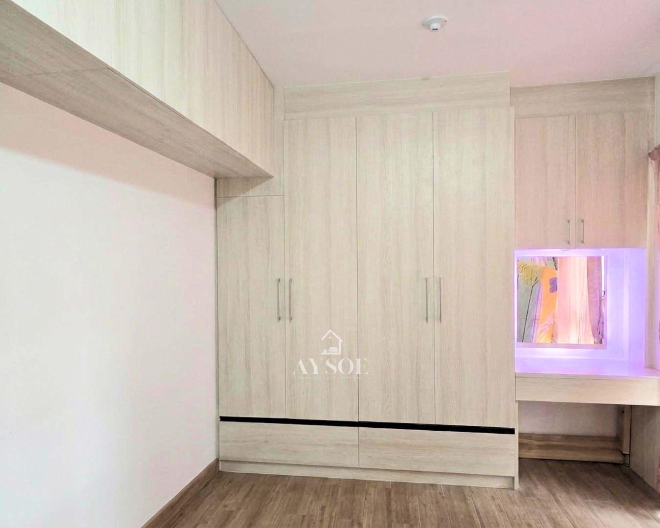 A custom light oak bedroom set with a tall four-door wardrobe, two bottom drawers, overhead cabinets, and a built-in vanity with an LED mirror. Lots of storage in one clean design.