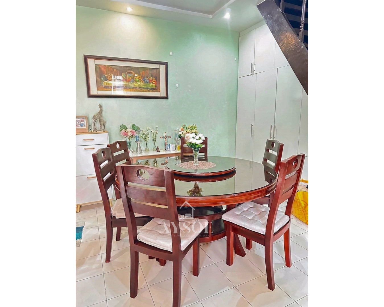 A round 6-seater dining set with a glass tabletop, a built-in rotating lazy Susan, a solid wood mahogany-finish base, and ladder-back chairs with soft tufted cushions.