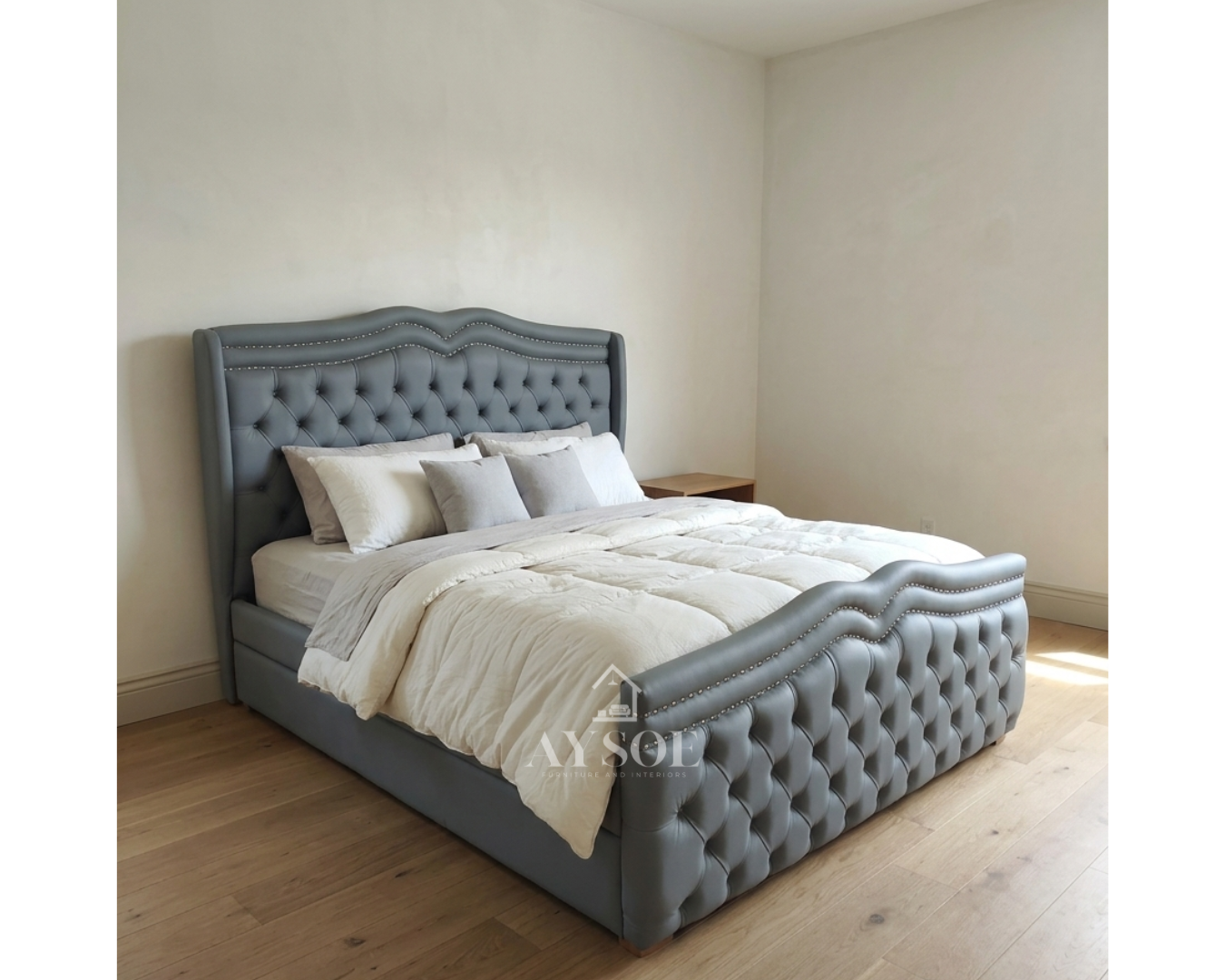 A luxurious bed frame in slate blue-grey leatherette, with a tall tufted wingback headboard, a matching footboard, nailhead trim, and a roll-out trundle drawer. Elegant and space-saving.