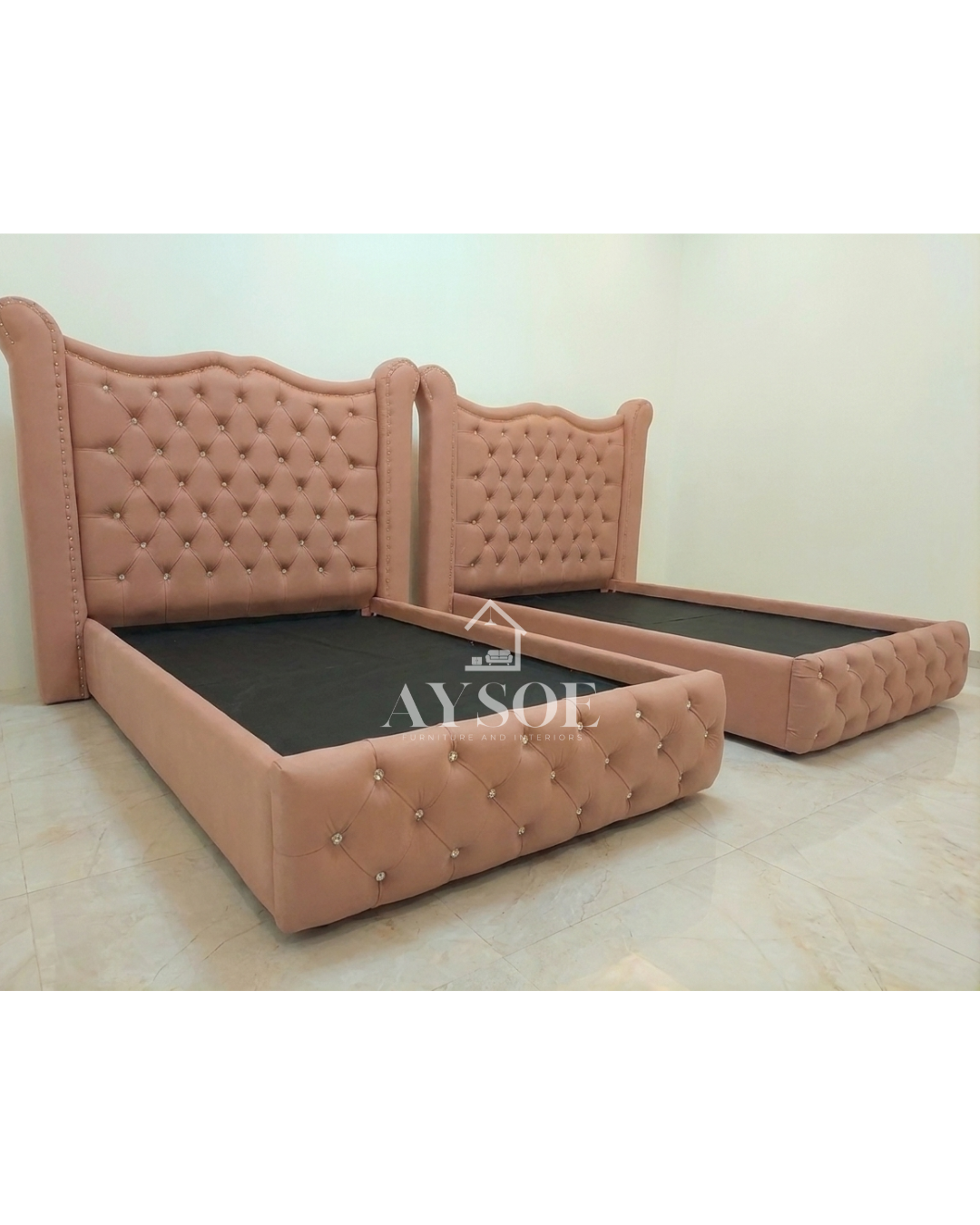A set of two single beds in blush pink leatherette, with tall wingback headboards, crystal buttons, and tufted footboards. Elegant, matching, and perfect for shared rooms.