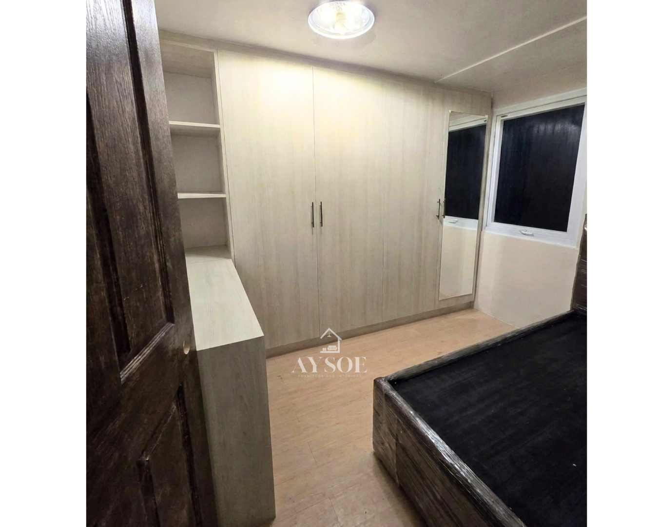 A custom light oak wardrobe with four full-height doors, a full-length mirror, built-in open shelves, and a desk counter. Complete bedroom storage in one clean design.