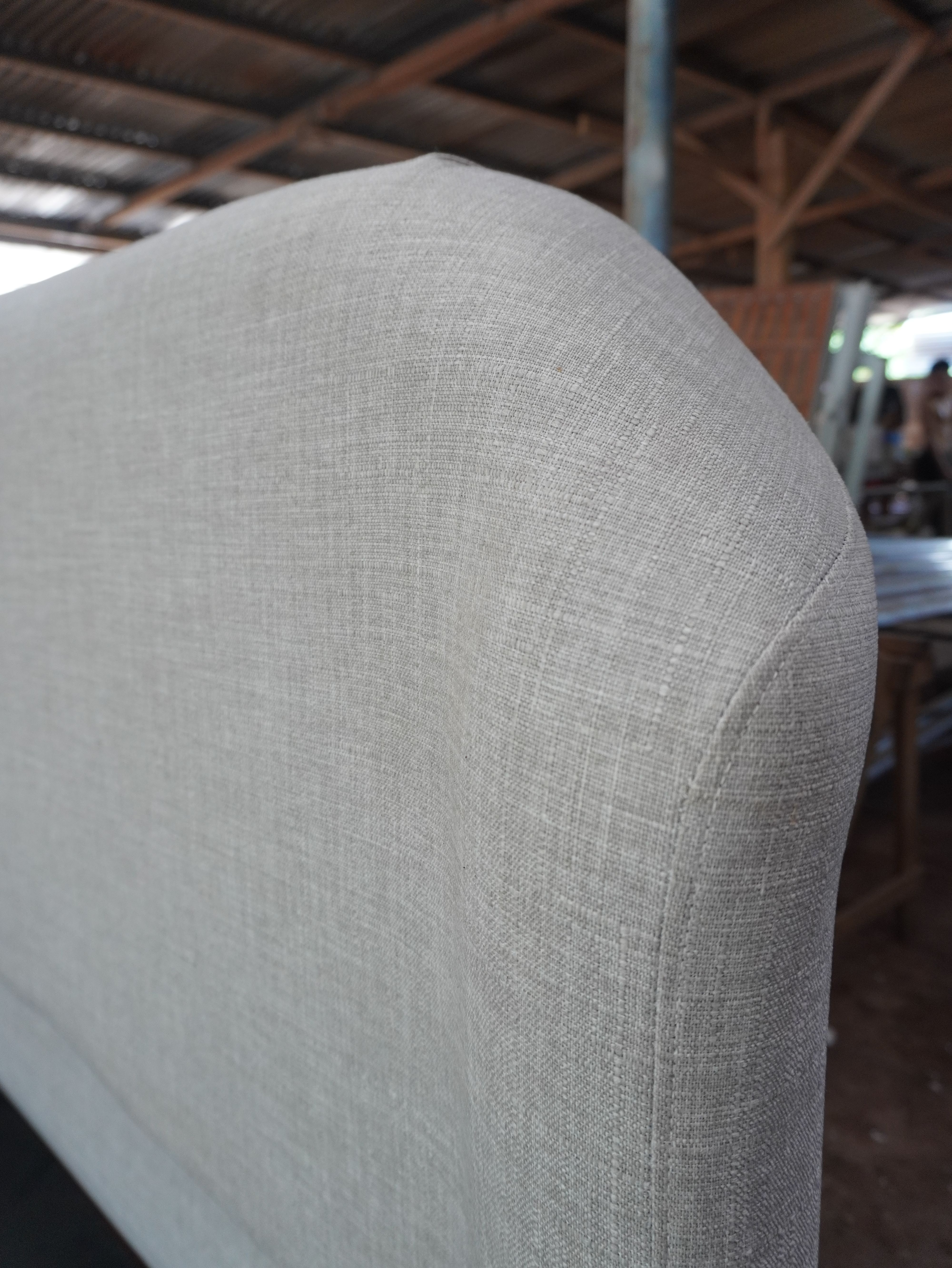 A clean, minimalist upholstered bed in light woven linen-style fabric, with a soft rounded headboard and a fully wrapped, low-profile frame. Calm, neutral, and easy to style.