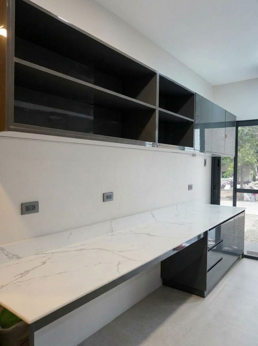 A sleek single-wall kitchen in high-gloss charcoal with a Calacatta-style marble backsplash. Handleless cabinetry, integrated appliances, and warm under-cabinet lighting give it a clean, modern look.