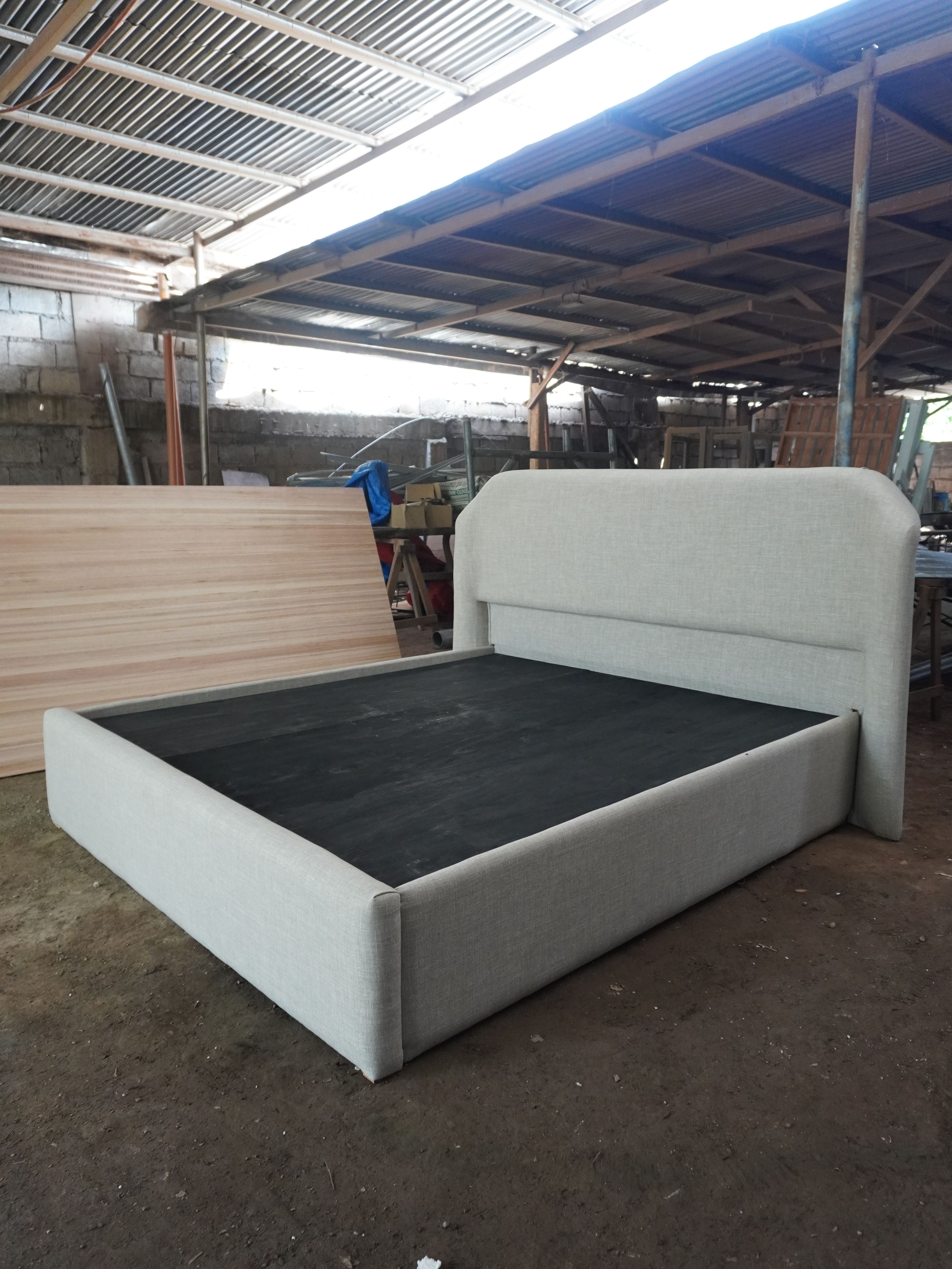 A clean, minimalist upholstered bed in light woven linen-style fabric, with a soft rounded headboard and a fully wrapped, low-profile frame. Calm, neutral, and easy to style.