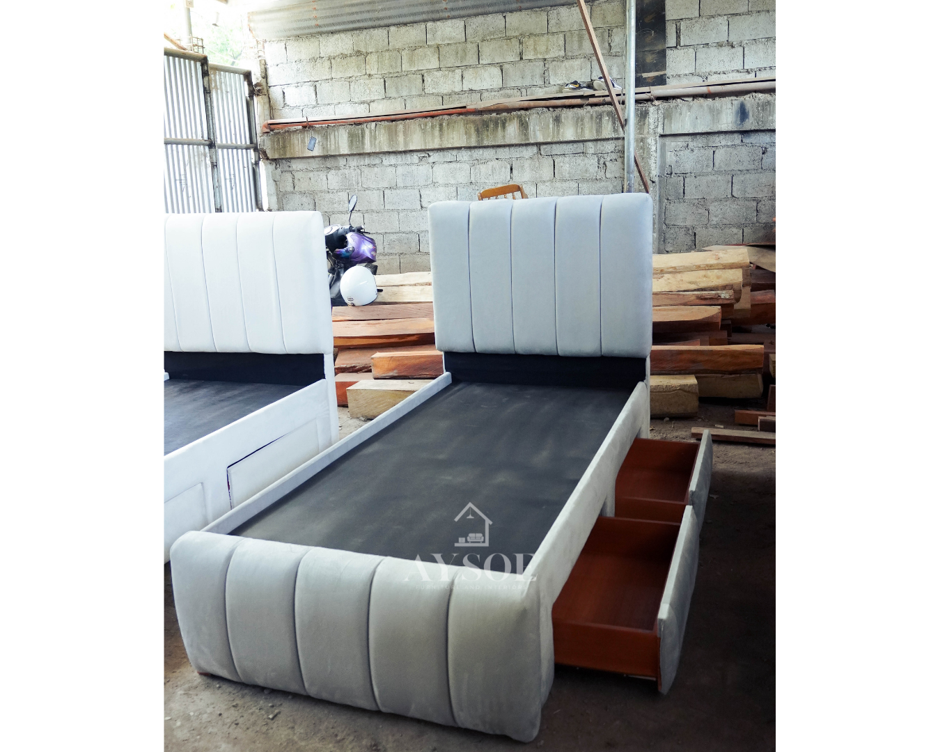 A single bed frame upholstered in soft light grey fabric, with a channel-tufted headboard and footboard and two roomy pull-out drawers. Stylish and space-saving.