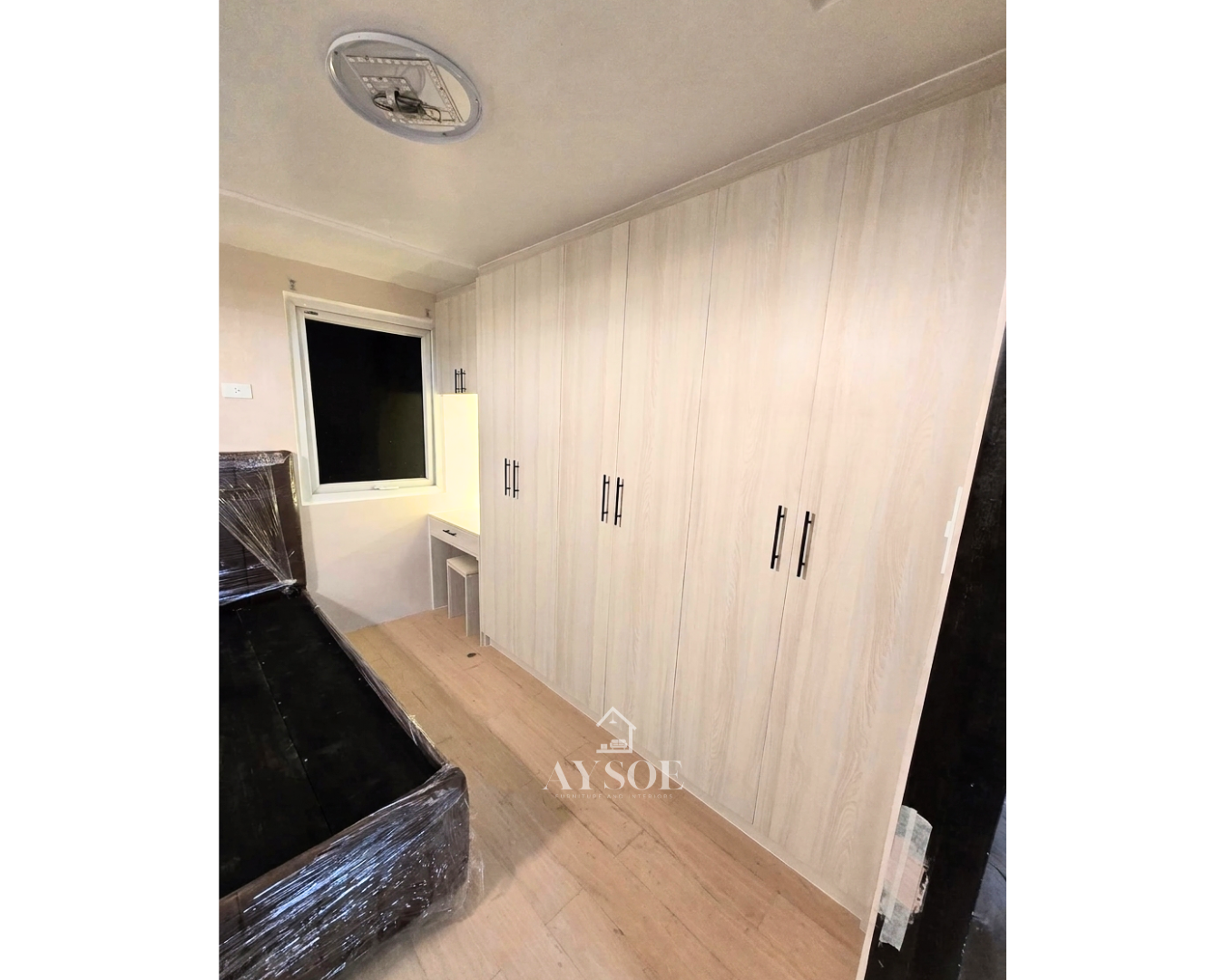 A custom light oak wardrobe with six full-height doors, a built-in vanity desk with LED lighting, and an overhead cabinet. Lots of storage in one clean design.