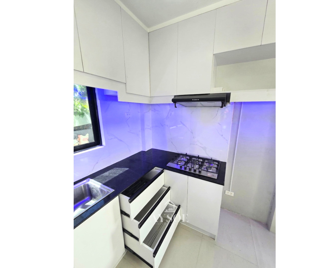 A modern L-shaped kitchen set with glossy white cabinets, a dark countertop, a marble-look backsplash, and a wood island counter with drawers. Plenty of storage in a clean, bright design.