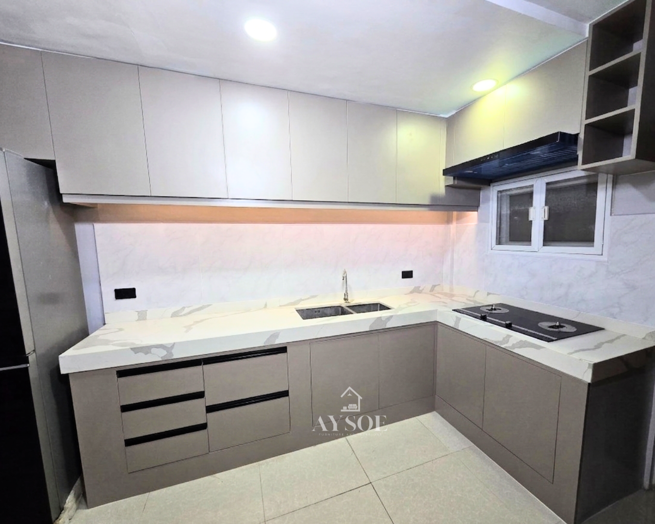 A modern L-shaped kitchen set with cream upper cabinets, taupe lower cabinets, and a marble-look countertop. Handleless, bright, and full of storage.