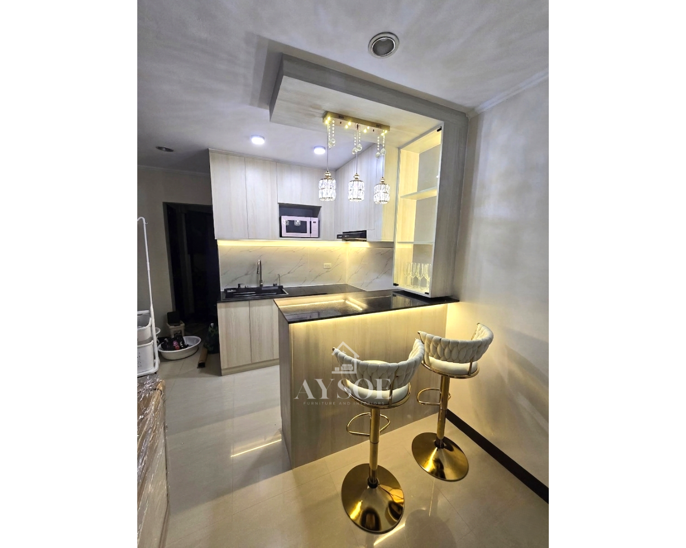 A compact light oak kitchen with a marble-look backsplash, breakfast bar, and lit glass display cabinet.